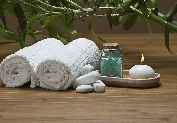 Toallas blancas enrolladas, sales de baño azules, vela encendida y bambú, ideal para recuperar toallas ásperas y disfrutar de un momento de spa.