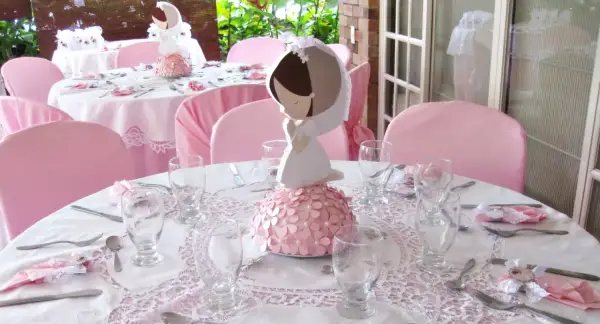 Detalle de decoración comunión niña casera con centros de mesa de comunión y mesas vestidas de rosa.