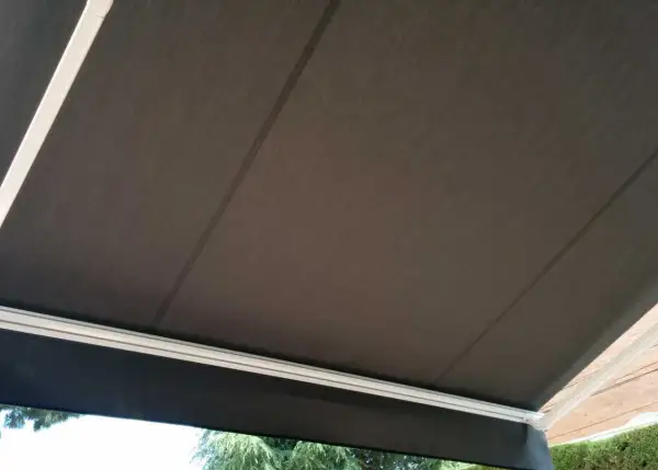 Toldo de acrílico tela oscura, con estructura blanca, protegiendo del sol.