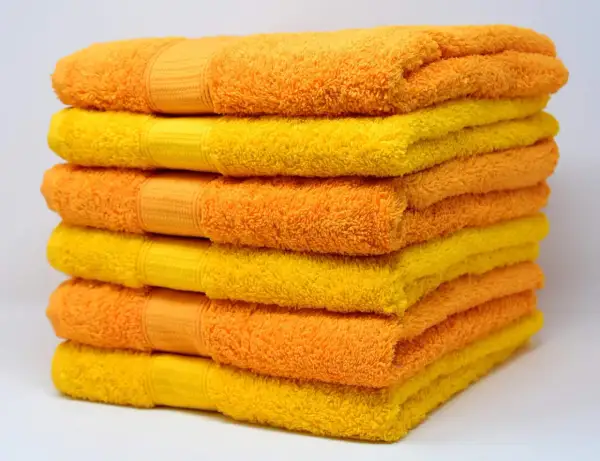 Pila de toallas suaves y esponjosas en tonos naranja y amarillo, listas para un baño reconfortante.