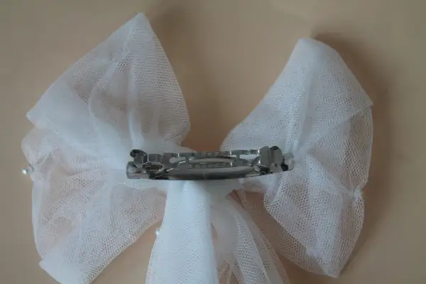 Un delicado lazo de tul blanco, adornado con perlas, sujeto por una pinza plateada.