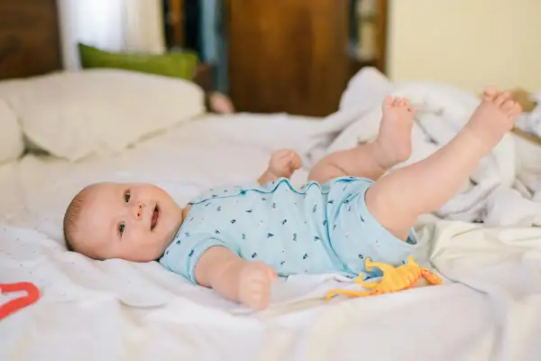 Mi bebé de 2 meses se voltea, sonriendo y jugando con un dinosaurio de juguete en la cama.