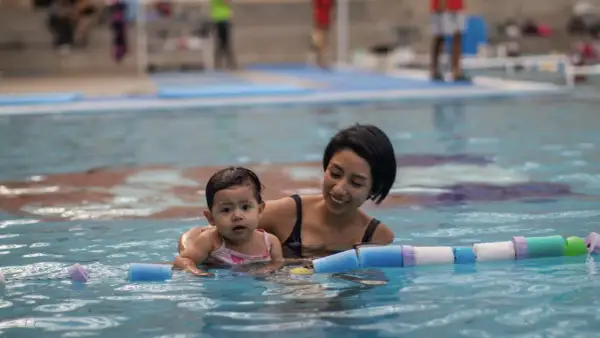 Madre sonriente enseña a su bebé natación para niños en la piscina, rodeados de flotadores.
