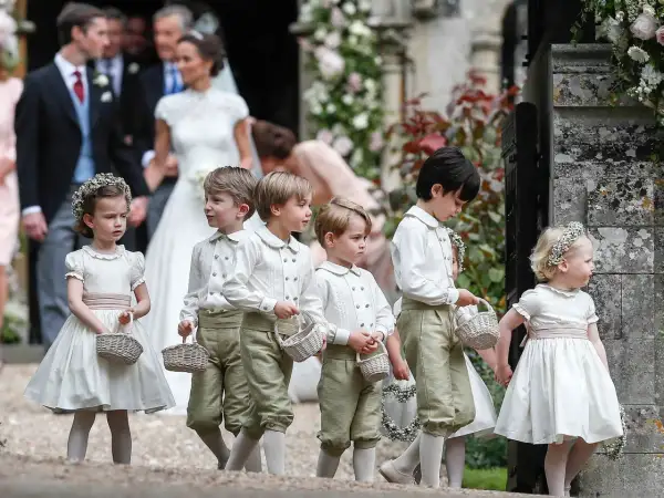Niños y niñas con trajes de época, portando cestas, son pajes en una boda.