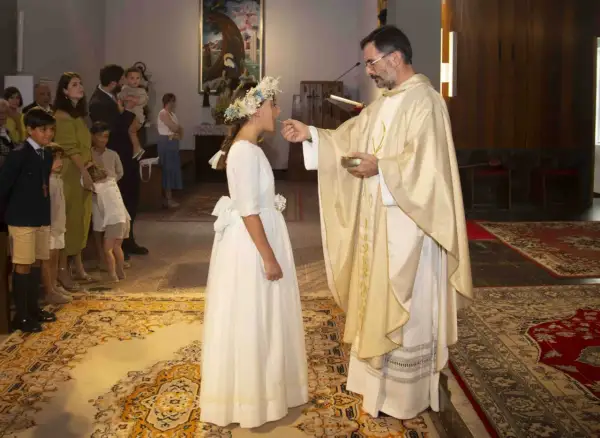 Niña recibe la comunión, un momento especial que marca a qué edad se hace la comunión. Familiares observan.