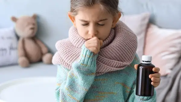 Niña con tos y bufanda, sosteniendo un frasco de medicina. Una imagen que ilustra cómo calmar la tos en niños.