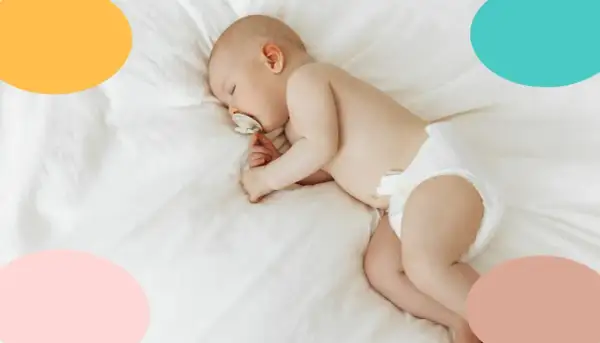 Un tierno bebé duerme de lado, con un chupete en la boca, envuelto en una suave manta blanca.