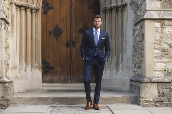 Hombre con traje azul marino, camisa blanca y corbata a cuadros, listo para saber qué hay que llevar a la iglesia para un bautizo.