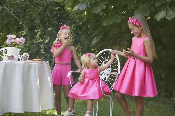 Niñas con vestidos fucsia, una con un fajín para vestido niña, disfrutan de un té en el jardín.