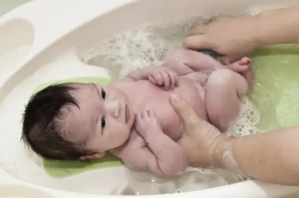 Un bebé sonriente disfruta de su primer baño. Aprende cuando bañar a un recién nacido con este tierno momento.