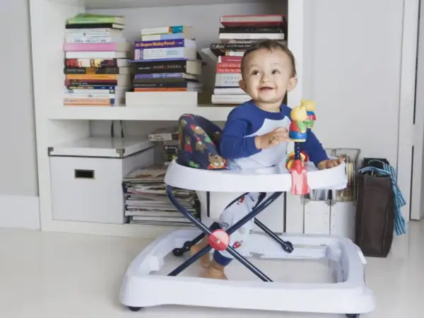 Bebé sonriente en andador, rodeado de libros. Posibles consecuencias del uso del andador en bebés.