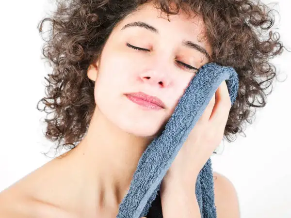 Mujer con rizos oscuros se seca la cara con toallas suaves y con buen olor, disfrutando de un momento de frescura.