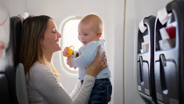 Madre sonríe a su bebé en un avión, jugando con un sonajero. Viajar con bebés puede ser una aventura alegre.