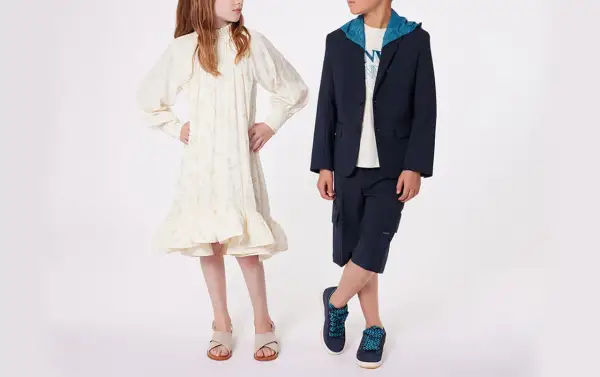 Niño y niña posan con atuendos elegantes. Ideas para como vestir a un niño de 14 años para una boda: traje azul marino con capota y bermudas.